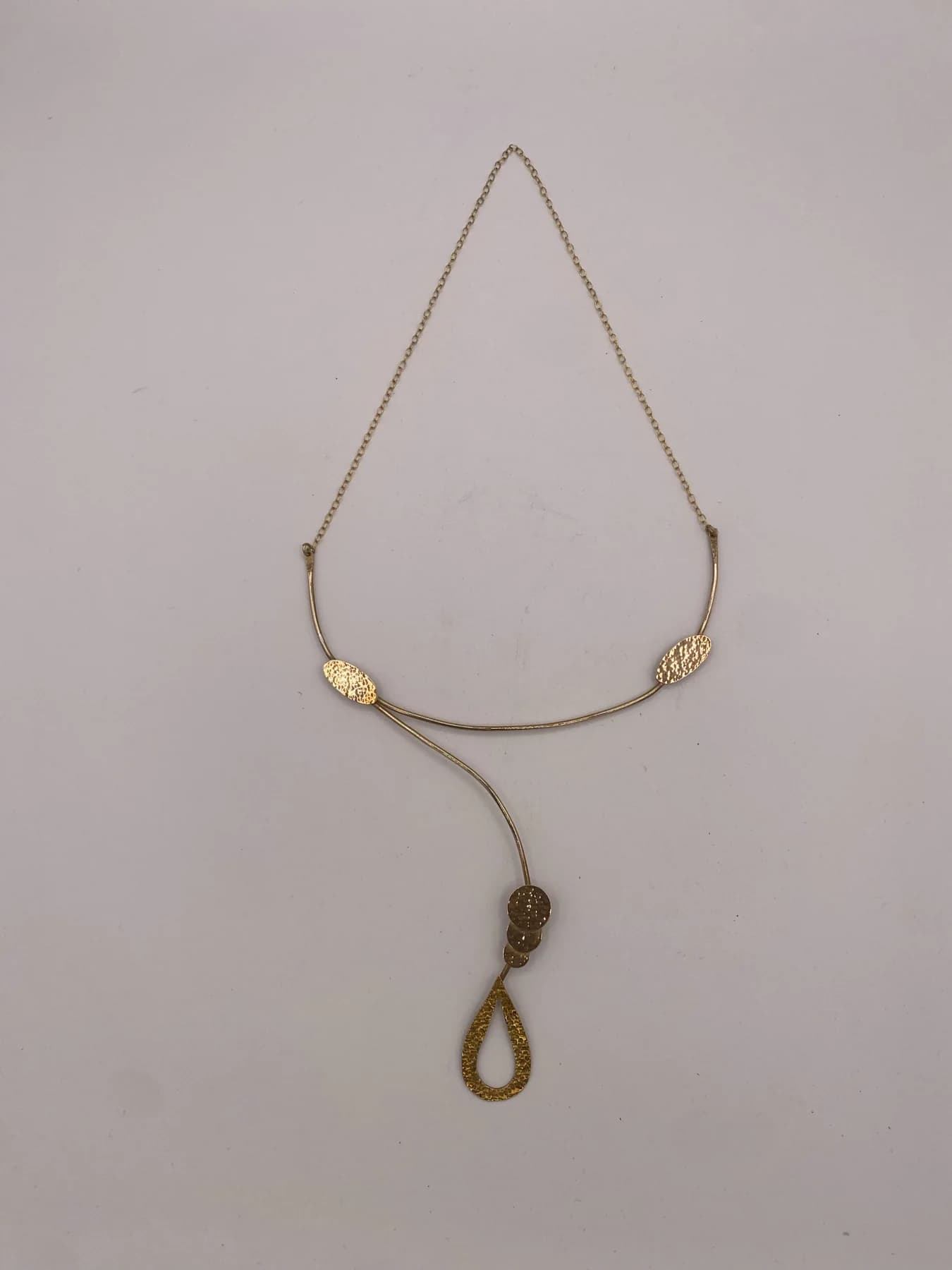 Long necklace laid out on a pale surface, with a loop-shaped pendant.